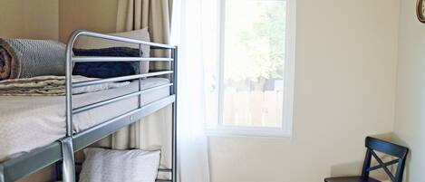 A bunk bed with a window, a chair, and a curtain.