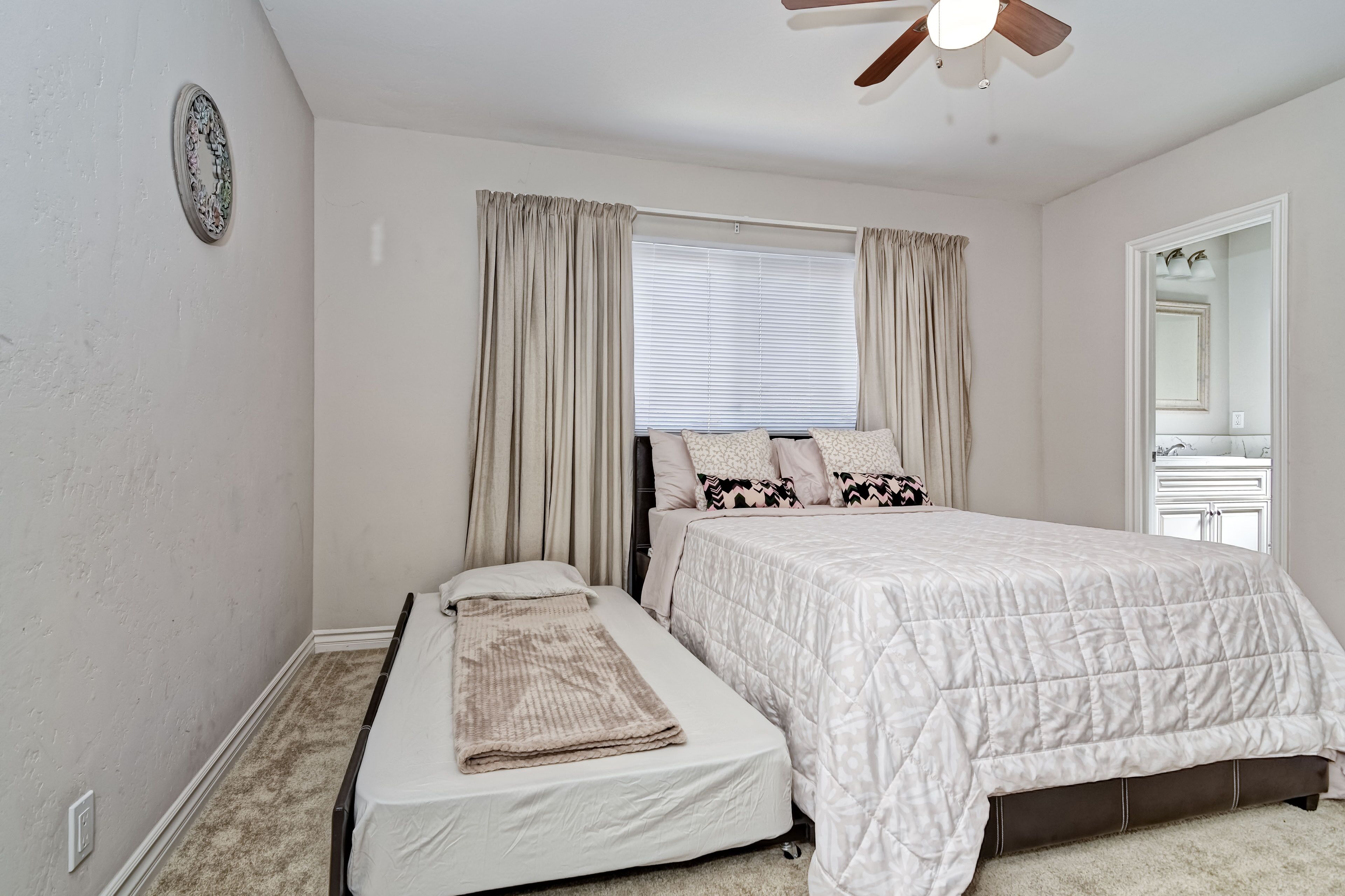 A bedroom with a single bed, a smaller bed, a ceiling fan, and a window with curtains.