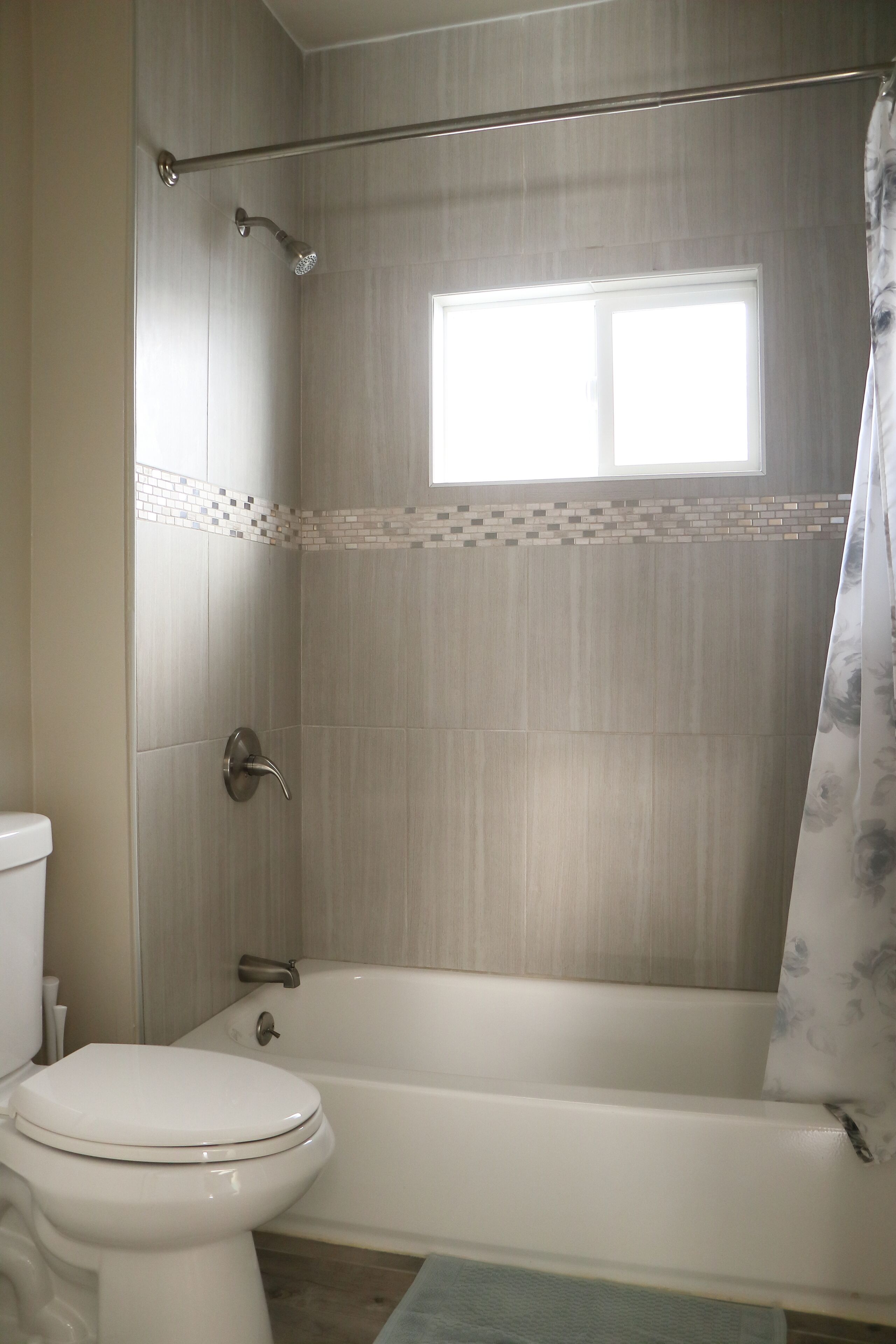 A bathroom with a toilet, bathtub, shower, and a window.