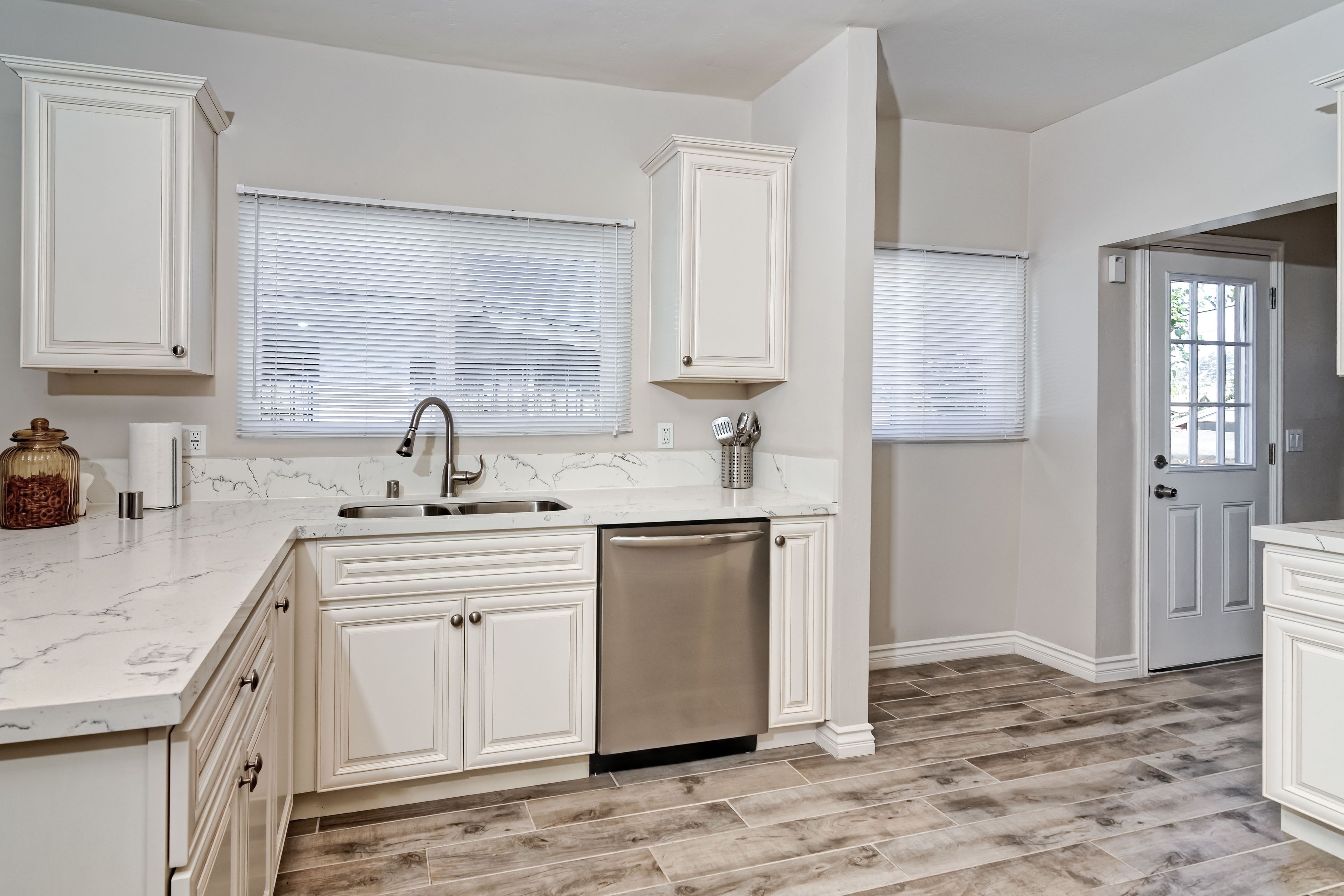 A kitchen with white cabinetry, a stainless steel dishwasher, and a marble countertop.