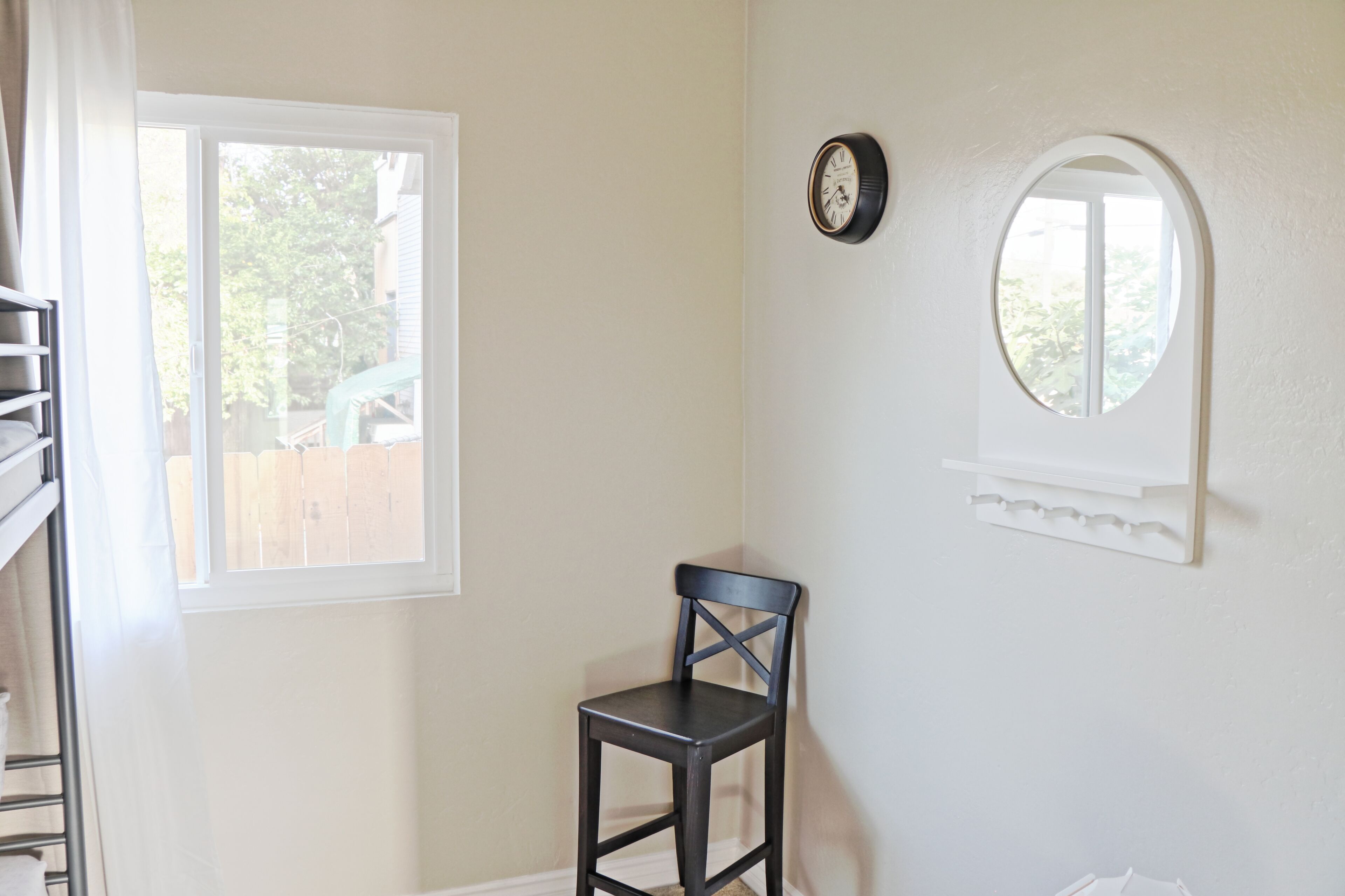 Una habitación con ventana, un reloj de pared y una silla.
