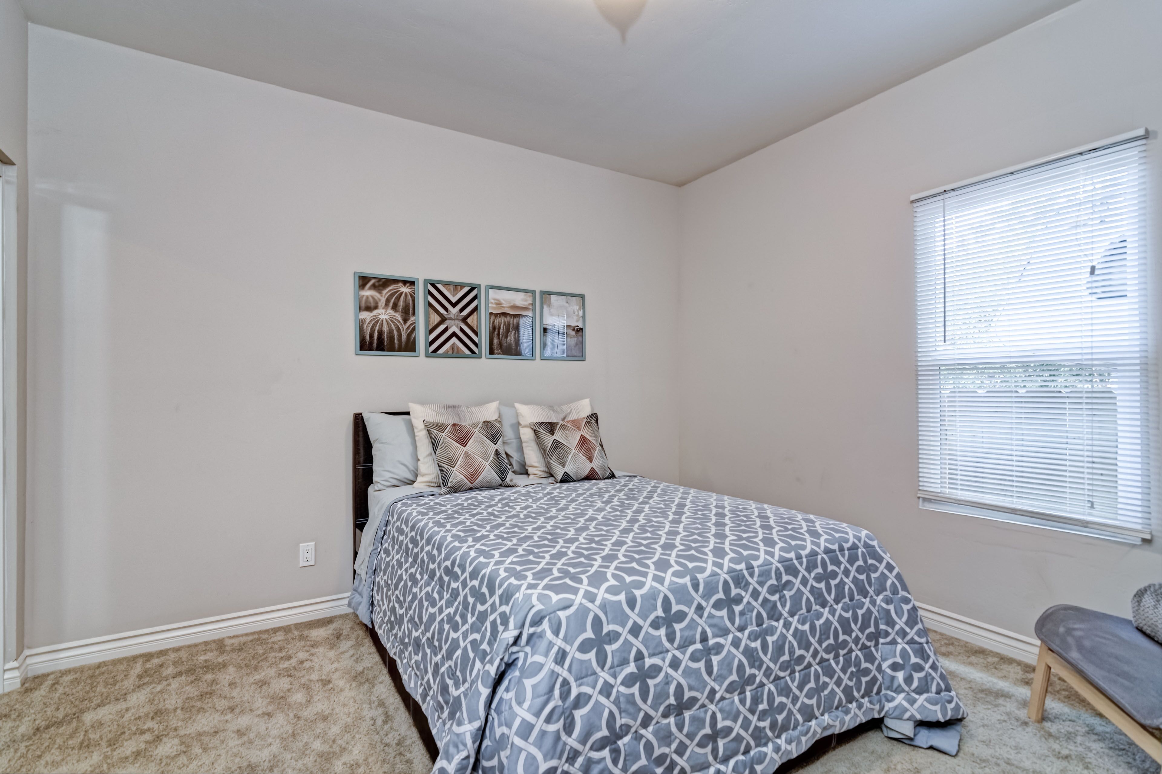 A bedroom with a bed, a window with blinds, and three wall-mounted pictures.
