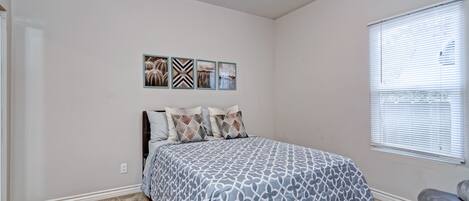 A bedroom with a bed, a window with blinds, and three wall-mounted pictures.