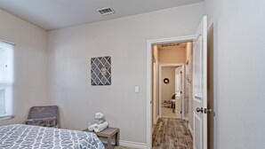A bedroom with a bed, a small table with towels, a chair, a picture on the wall, and a door leading to a hallway. - 4bd / 2bth private parking, 8 min to Gaslamp, Zoo (San Diego)