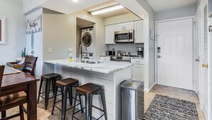 Cocina compacta con una isla central, lavadora, microondas y pileta.