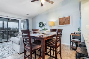 A dining area with a wooden table and chairs, a ceiling fan, and a view of the outdoors through large windows.