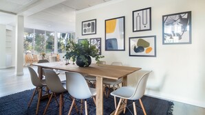 A modern dining area with a wooden table and grey chairs, surrounded by abstract art on the wall.