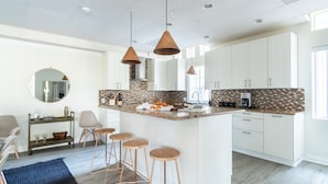 A modern kitchen with a central island, bar stools, pendant lighting, and a backsplash with a mosaic tile pattern.
