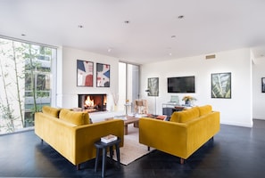 Un salon moderne avec une cheminée, des canapés jaunes et de grandes fenêtres.