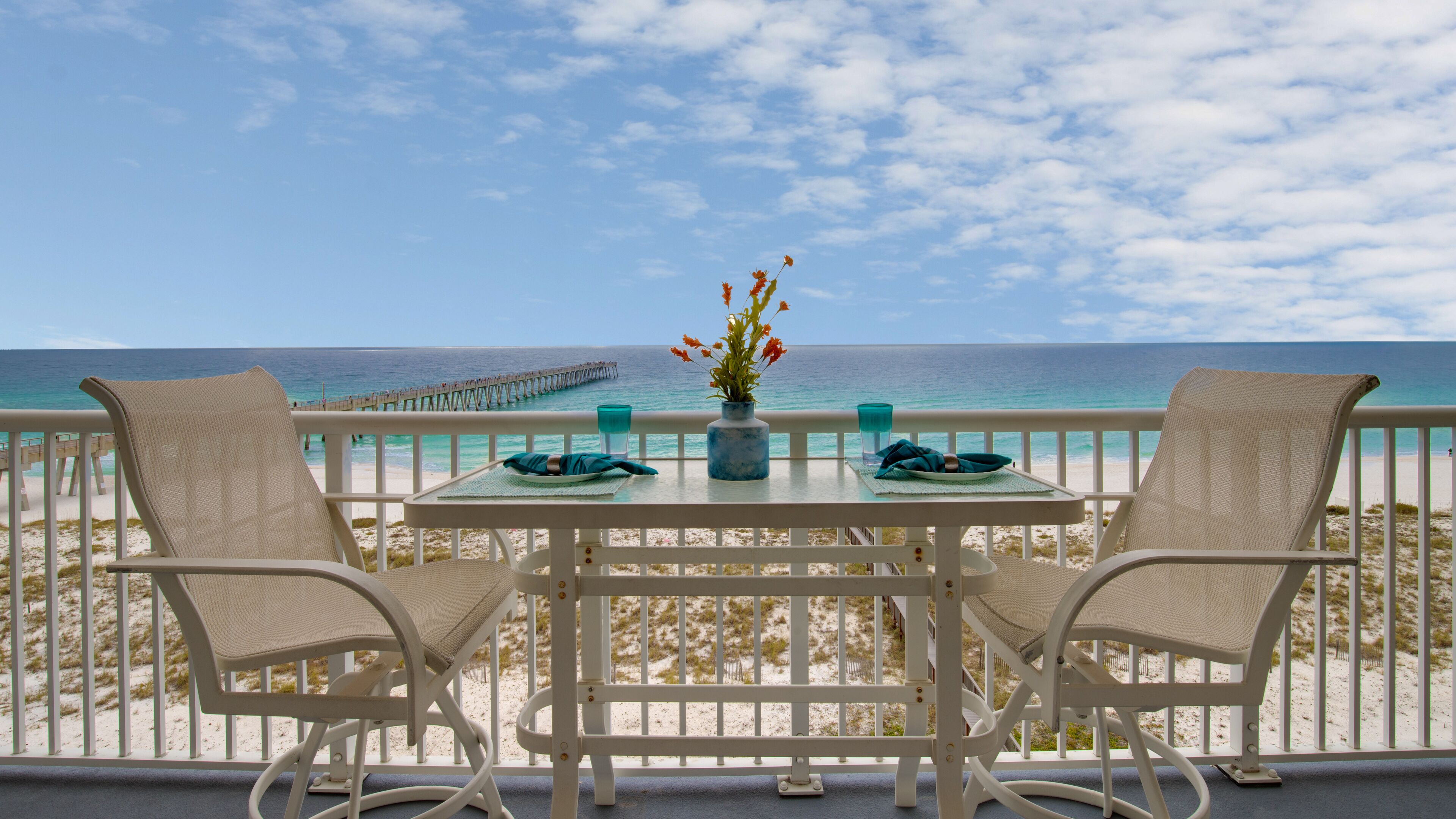 A balcony with a table and chairs overlooking a beach and pier.