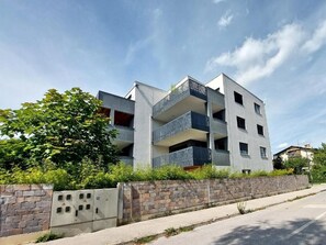 A multi-story residential building with balconies, a stone wall in front, and a clear sky. - Deluxe TIVOLI Suites (Ljubljana)