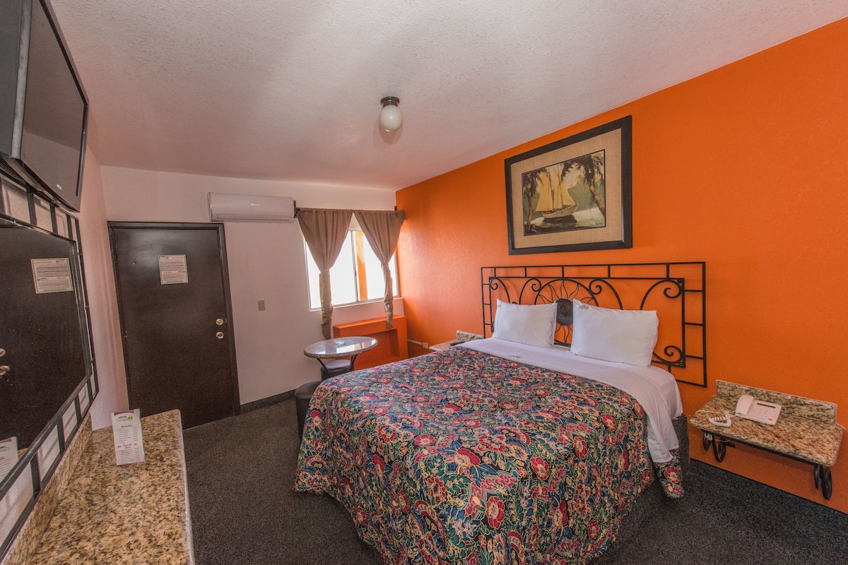 A hotel room with a bed, a desk, a chair, a window with curtains, and a door.