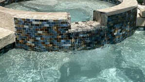 Une piscine dont le bord est orné de mosaïques et dont le pourtour est délimité par une bordure en pierre.