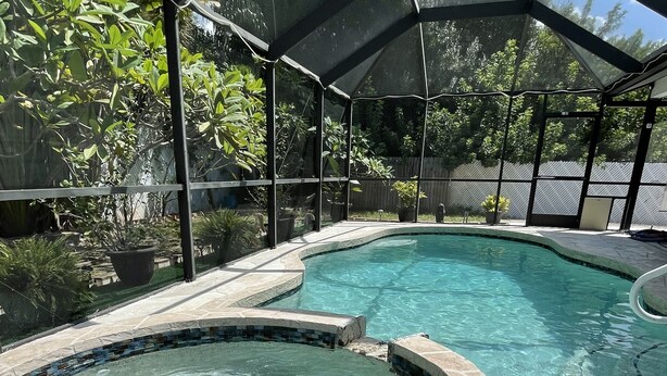 Une piscine à bord incurvé et un espace séparé avec un jacuzzi, le tout entouré d’une terrasse couverte et d’une clôture en métal.