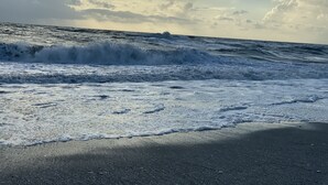 Une plage où les vagues se brisent sur le rivage, sous un ciel nuageux.