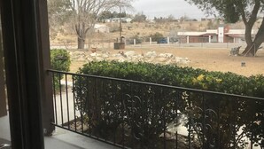 Vistall des d'un balcó amb barana metàl·lica, sobre un paisatge sec amb vegetació escassa i alguns edificis a la distància.