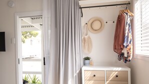 A bedroom with a bed, a dresser, a hat on the wall, and a window with blinds. - Little Palm Cabins (Lake Cathie)