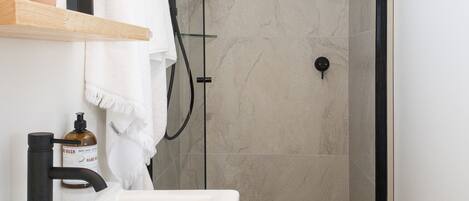A modern bathroom with a glass-enclosed shower, a white sink, and a wooden shelf with toiletries.
