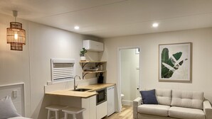 A modern, compact living space with a kitchenette, a sofa, and a bed. - Little Palm Cabins (Lake Cathie)