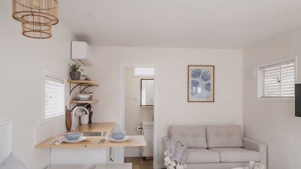 A modern, minimalist living space with a kitchen area, a sofa, and a small dining table. - Little Palm Cabins (Lake Cathie)