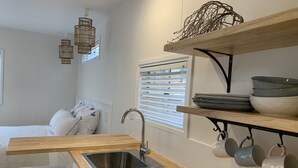 A compact kitchen with a wooden countertop, stainless steel sink, and hanging mugs. - Little Palm Cabins (Lake Cathie)