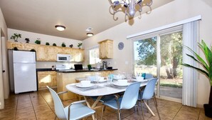 A modern kitchen with wooden cabinets, a white refrigerator, and a dining area with a round table and blue chairs.