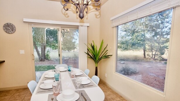 A dining area with a table set for six, a potted plant, and a view of trees through a window.
