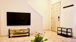 A living room with a flat-screen TV mounted on the wall, a wooden console table, a potted plant, and a door with a coat rack.