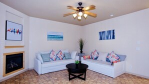 A living room with a white sofa, a black coffee table, a ceiling fan, and artwork on the walls.