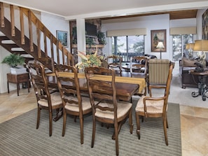 Uma sala de jantar ampla com mesa e cadeiras de madeira, uma escada e uma sala de estar aconchegante com sofá e televisão.