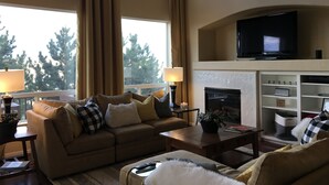 A living room with a sofa, coffee table, and a fireplace. There is a television mounted above the fireplace.