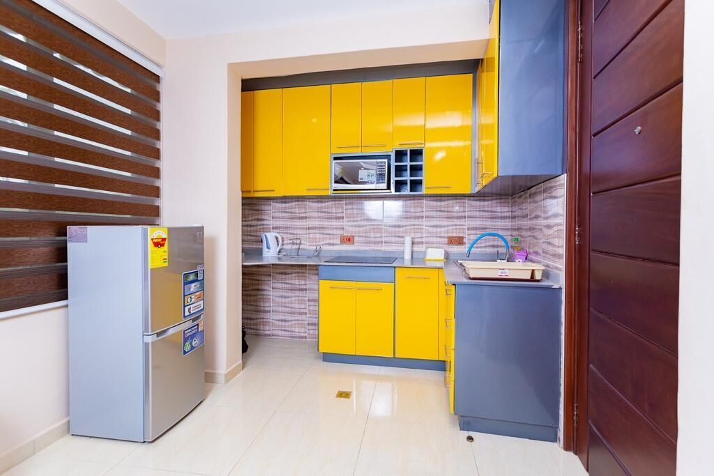 A compact kitchen with yellow cabinets, a built-in microwave, and a refrigerator.