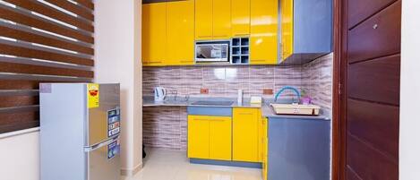 A compact kitchen with yellow cabinets, a built-in microwave, and a refrigerator.