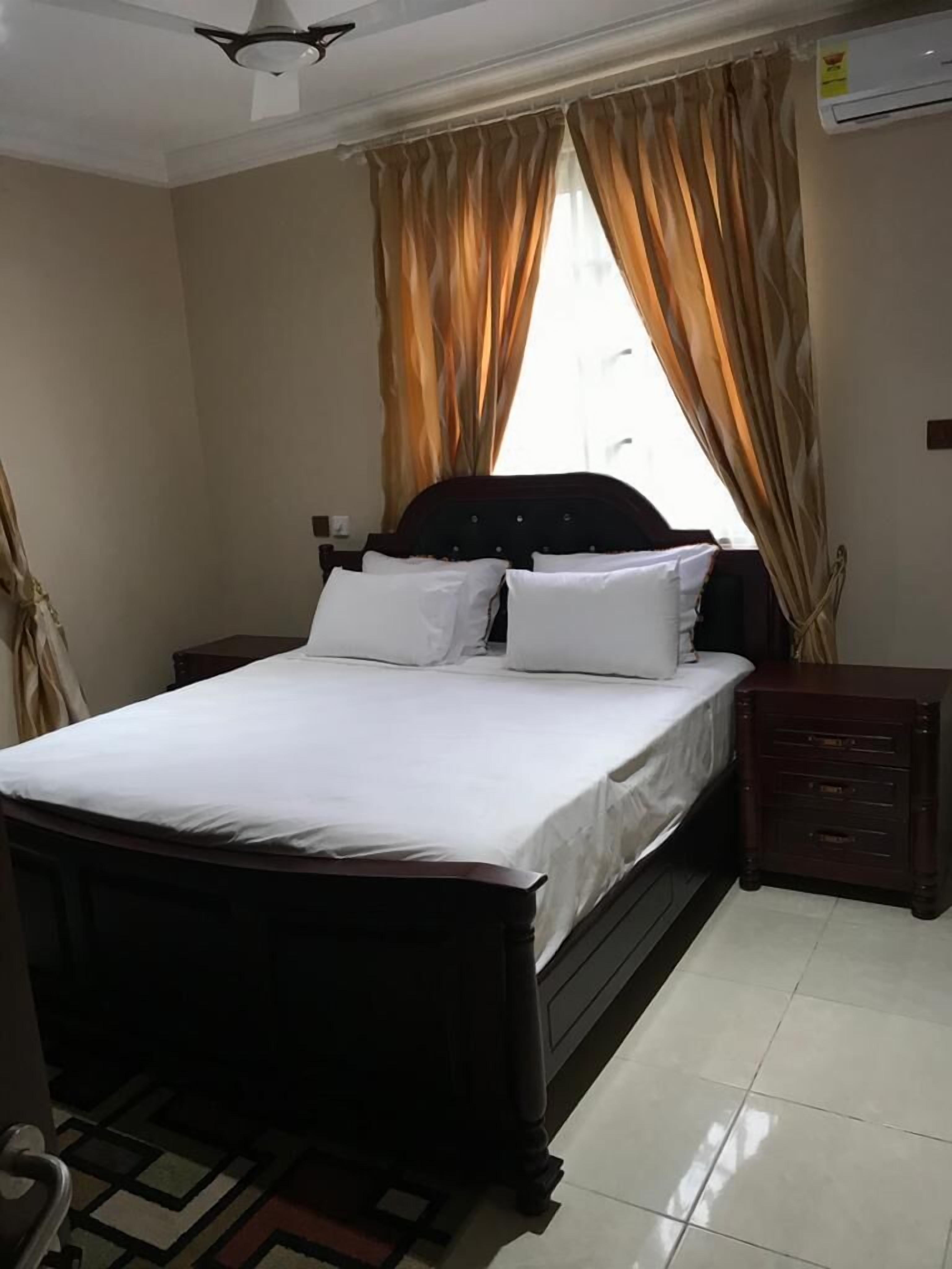 A bedroom with a bed, nightstands, a dresser, a ceiling fan, and a window with curtains.