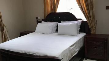 A bedroom with a bed, nightstands, a dresser, a ceiling fan, and a window with curtains.