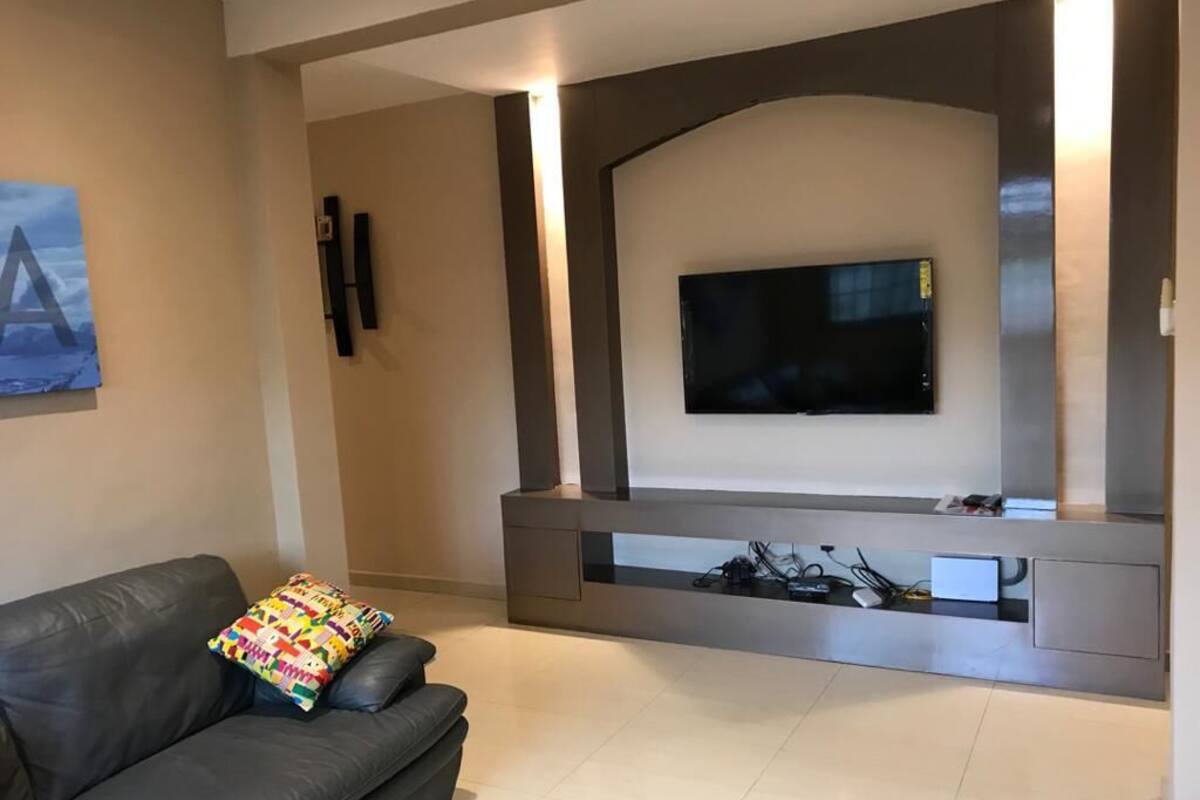 Uma sala de estar moderna com uma televisão de tela plana na parede, um sofá de couro escuro e uma mesa de centro de vidro.