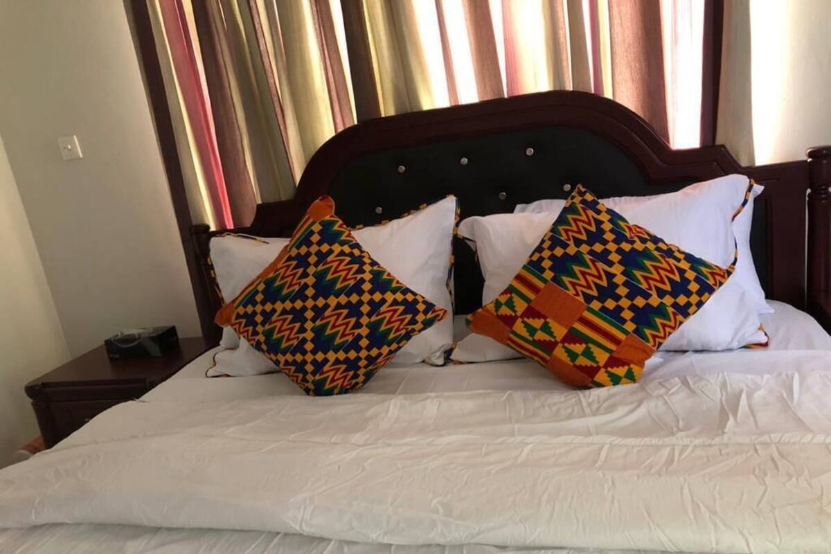Cama com roupa branca e dois travesseiros decorativos com padrões geométricos.