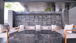 A modern outdoor seating area with a marble table and sofas, a textured wall, and a patterned ceiling. - LeGrant Suites Sukhumvit 11 Bangkok (Bangkok)