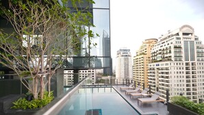 A rooftop infinity pool with lounge chairs and a view of surrounding high-rise buildings. - LeGrant Suites Sukhumvit 11 Bangkok (Bangkok)