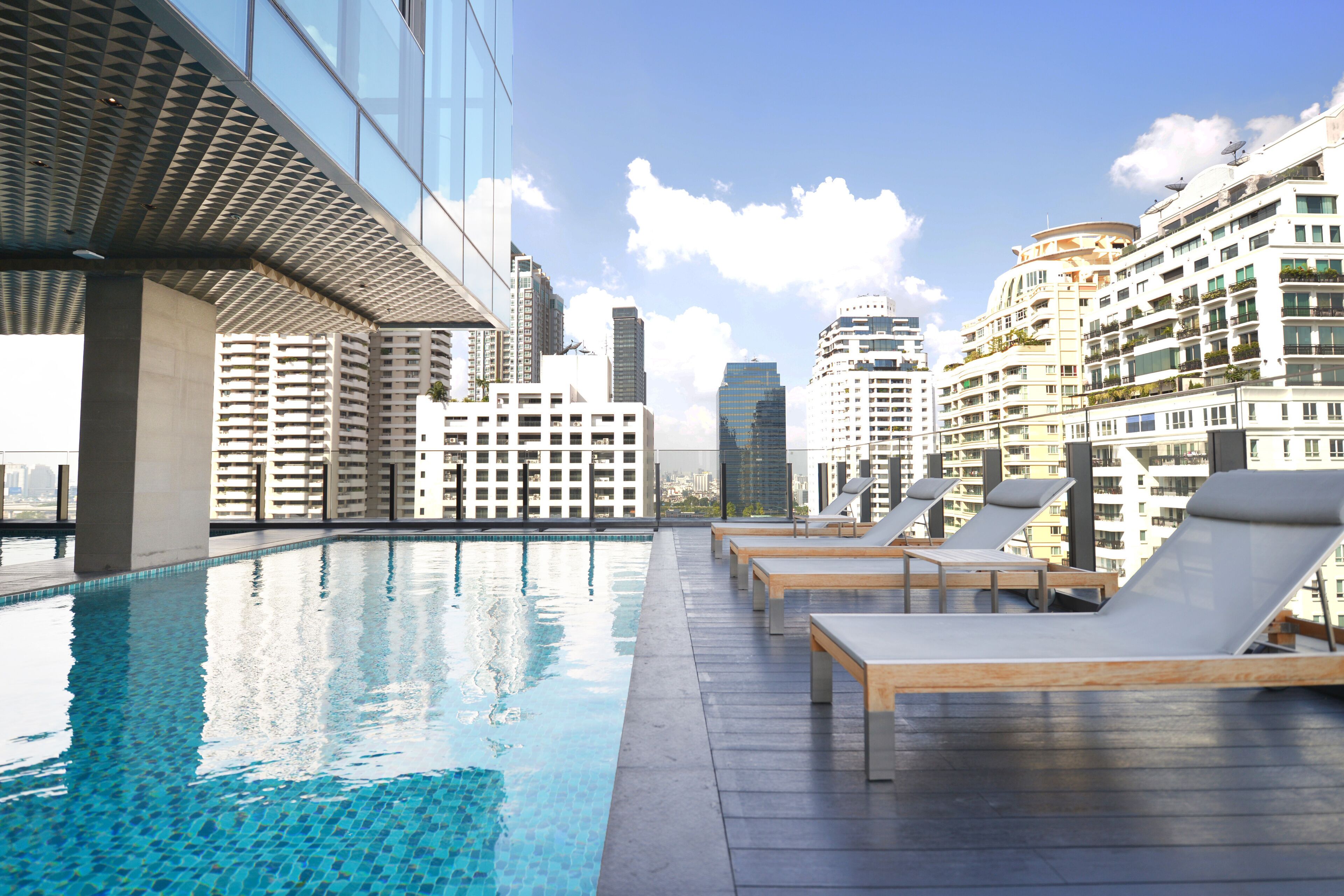Una piscina en la azotea con sillones de descanso, arquitectura moderna y el horizonte de la ciudad al fondo.
