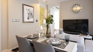 A modern dining area with a table set for four, a sofa, and a flat-screen TV. - LeGrant Suites Sukhumvit 11 Bangkok (Bangkok)