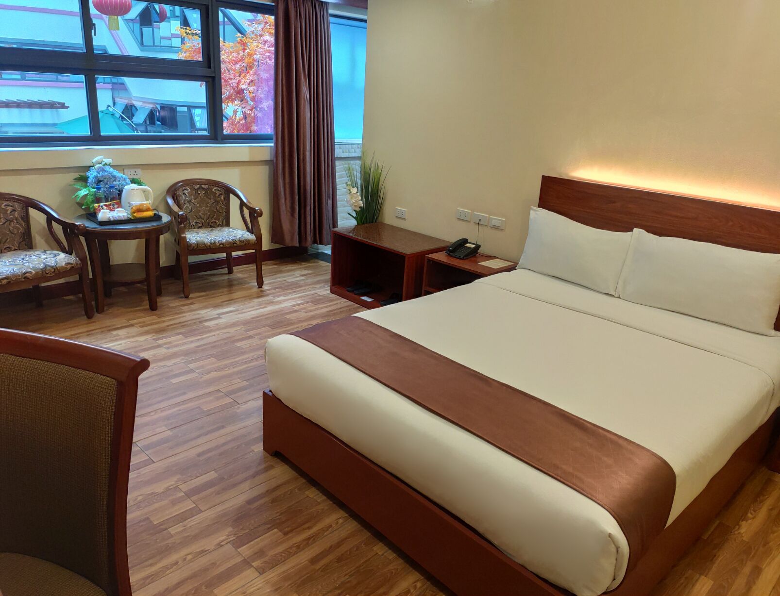 Habitación de hotel con una cama grande, dos sillones, una mesita con un jarrón y una mesita de noche con un teléfono.
