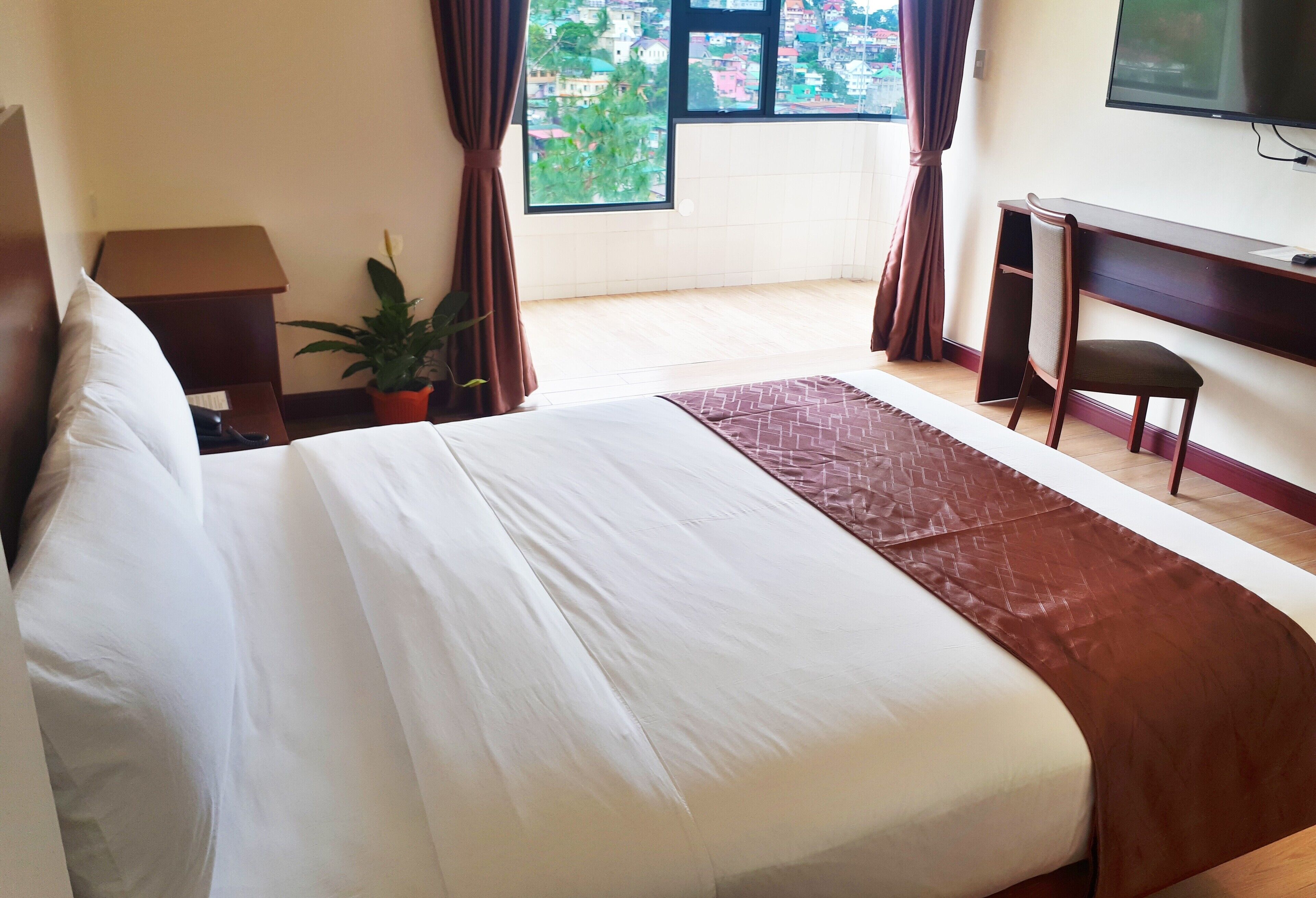Habitación de hotel con una cama grande, un escritorio, una silla, un televisor y una ventana con cortinas.