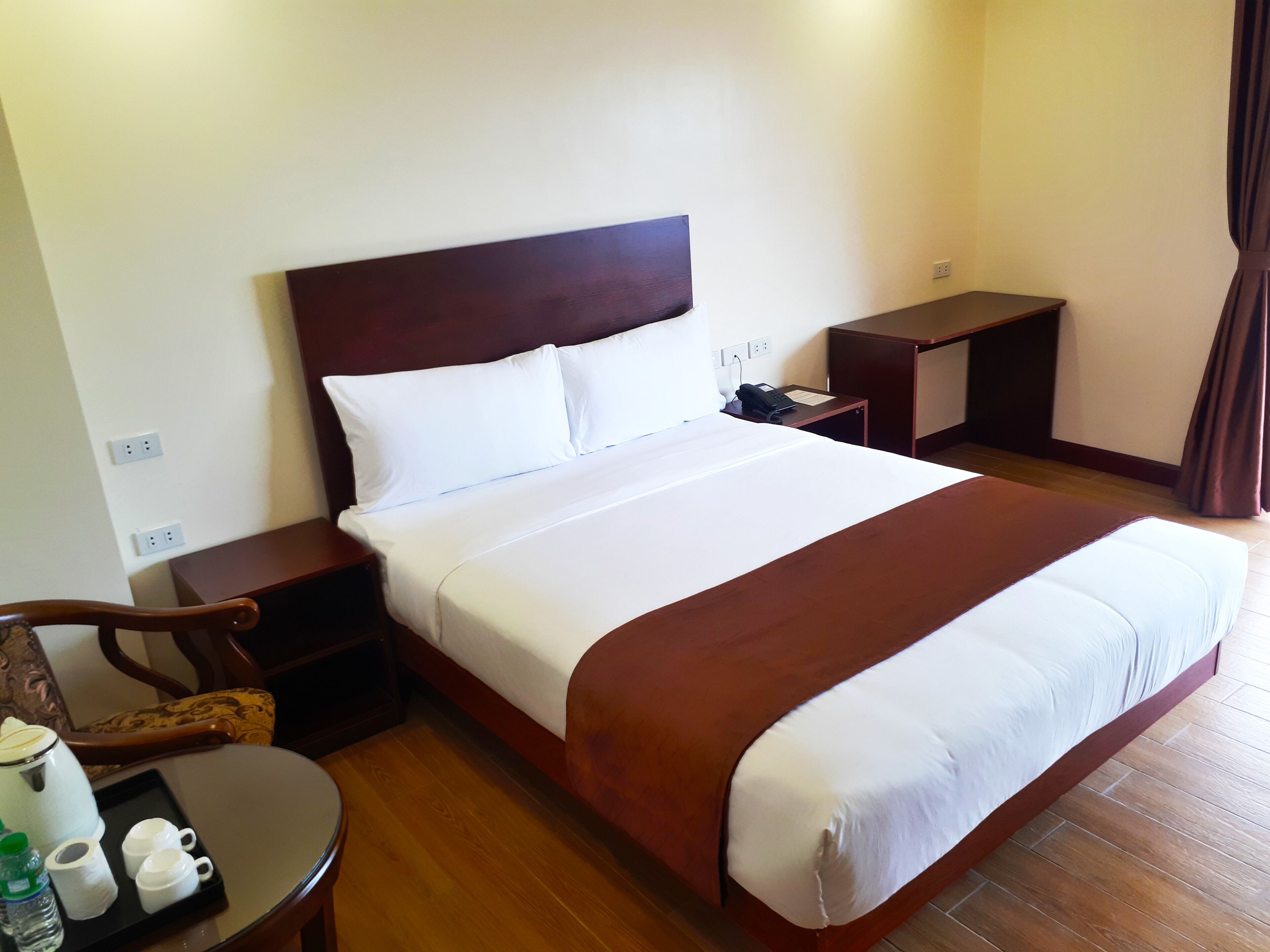 A hotel room with a large bed, a wooden nightstand, a desk, and a chair.
