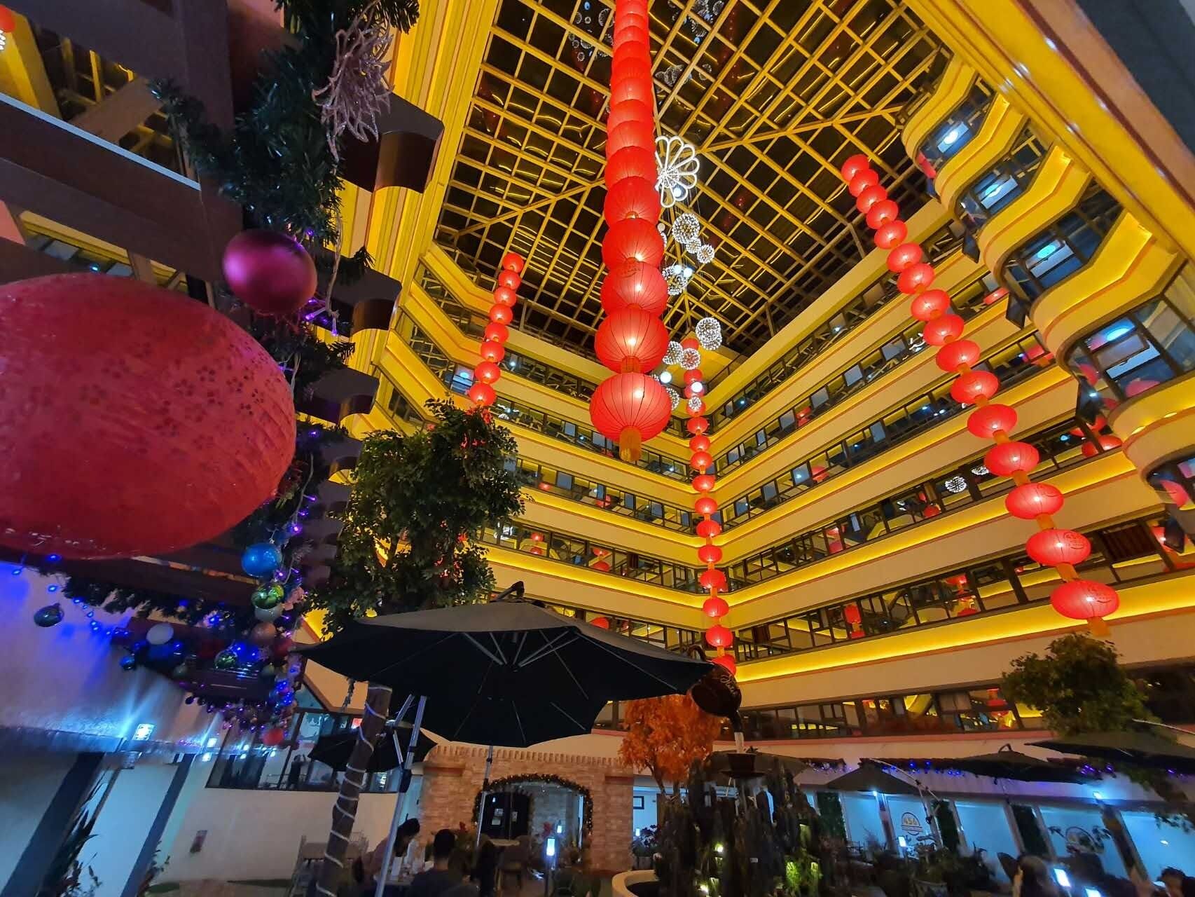 A multi-level atrium with a modern design, featuring a central column with red lanterns, a large umbrella, and a fountain.