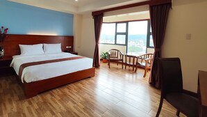 A hotel room with a large bed, wooden flooring, a view through a window, and a seating area with chairs and a table. - 456 Hotel (Baguio)