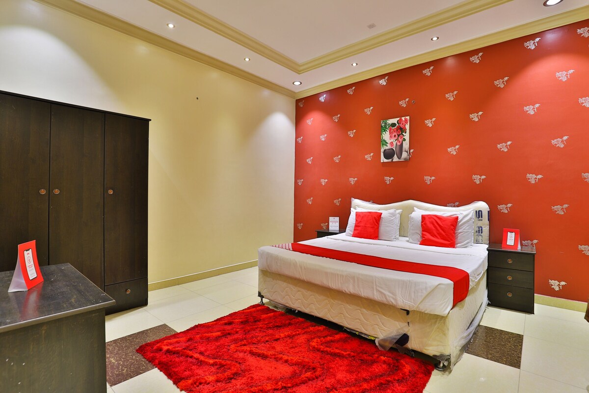 Ein Hotelzimmer mit Bett, Nachttisch, Schreibtisch und einem roten Teppich.