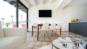A modern dining area with a large table, white chairs, and a flat-screen TV on the wall. - Luxury villa with pool situated near Ribera, Agrigento, Sicily – 6 pax (Ribera)