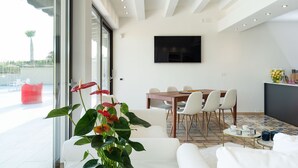 A modern living room with a dining area, large windows, and a flat-screen TV mounted on the wall. - Luxury villa with pool situated near Ribera, Agrigento, Sicily – 6 pax (Ribera)