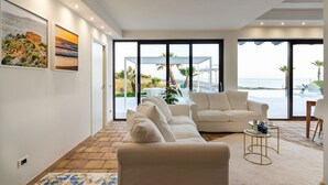 A modern living room with a beige sofa, a coffee table, and a view of the beach through large windows. - Luxury villa with pool situated near Ribera, Agrigento, Sicily – 6 pax (Ribera)